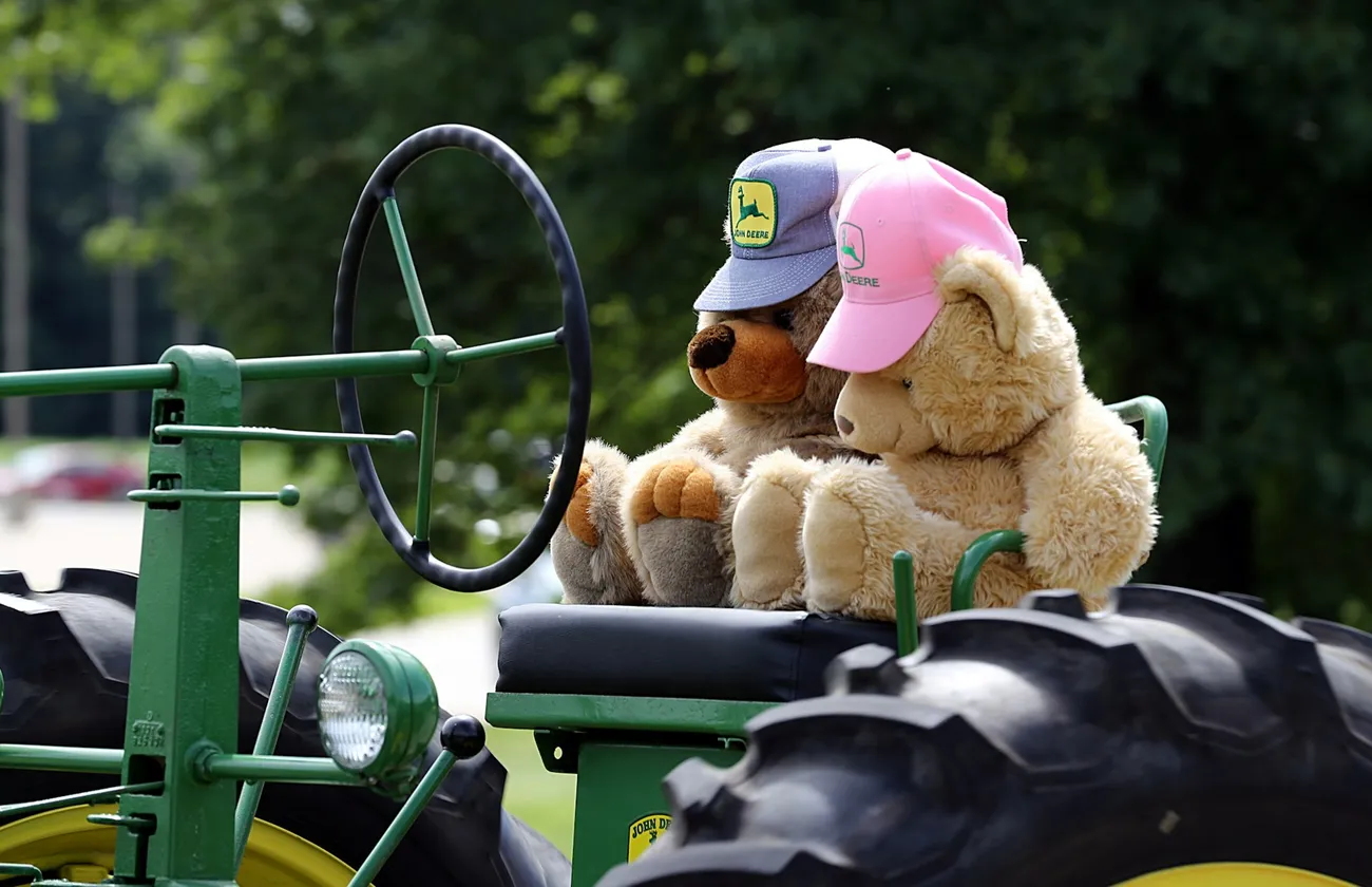 Zwei Teddybären mit Kappen sitzen auf einem alten grünen Traktor